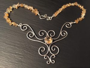 A silver citrine swirl necklace by Sandra Kerns. Swirls of silver around a central set citrine gem, with citrine stones threaded onto the necklace.